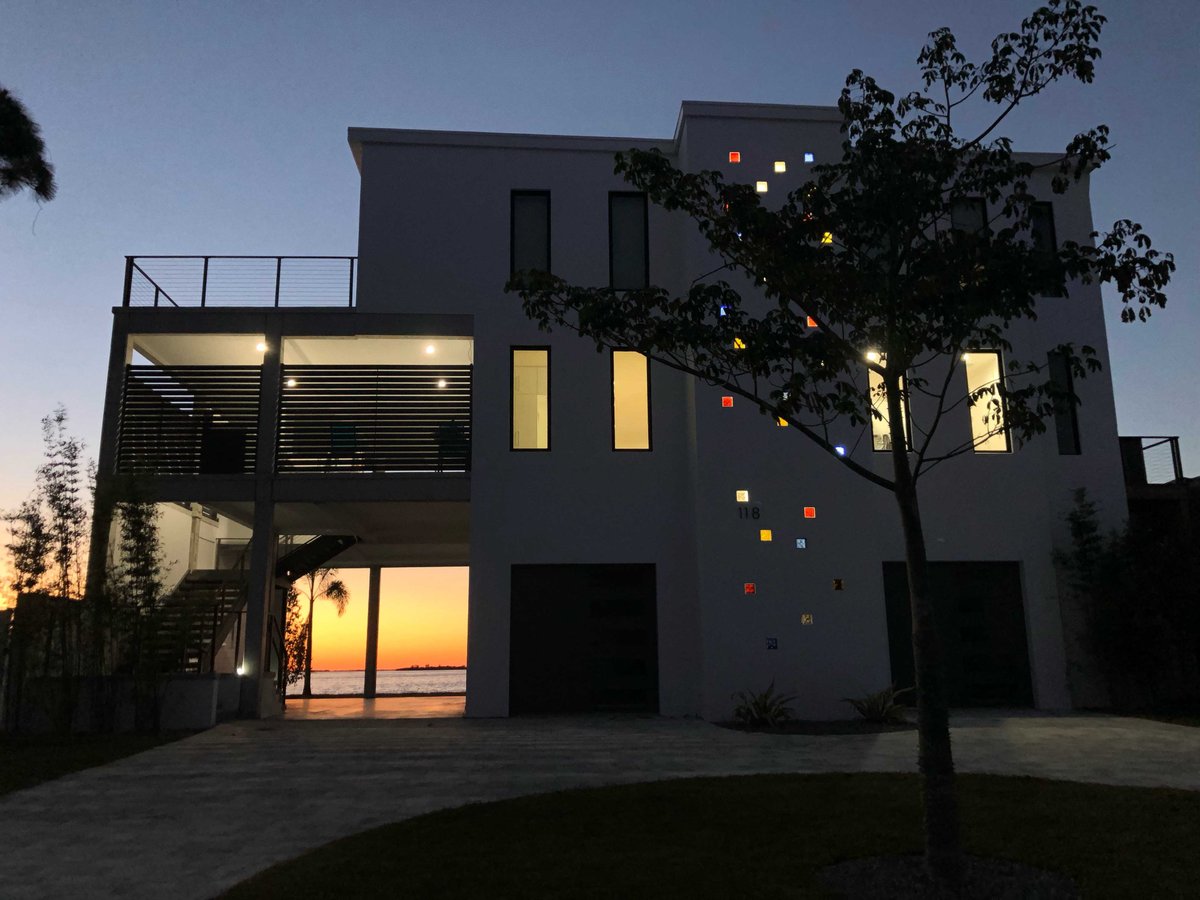 Image of front of modern white home at dusk with beautiful sunset cascading through open car port on side of home