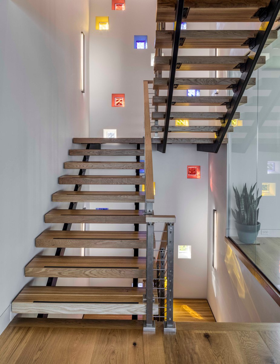 Image of open wooden stairs in modern white home with glass wall to one side of stairwell