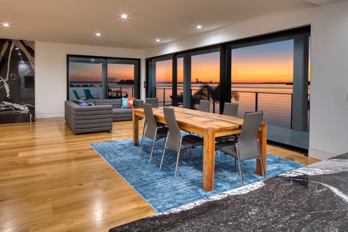 Image of modern open dining and living rooms with wooden flooring and expansive sliding glass doors to veranda