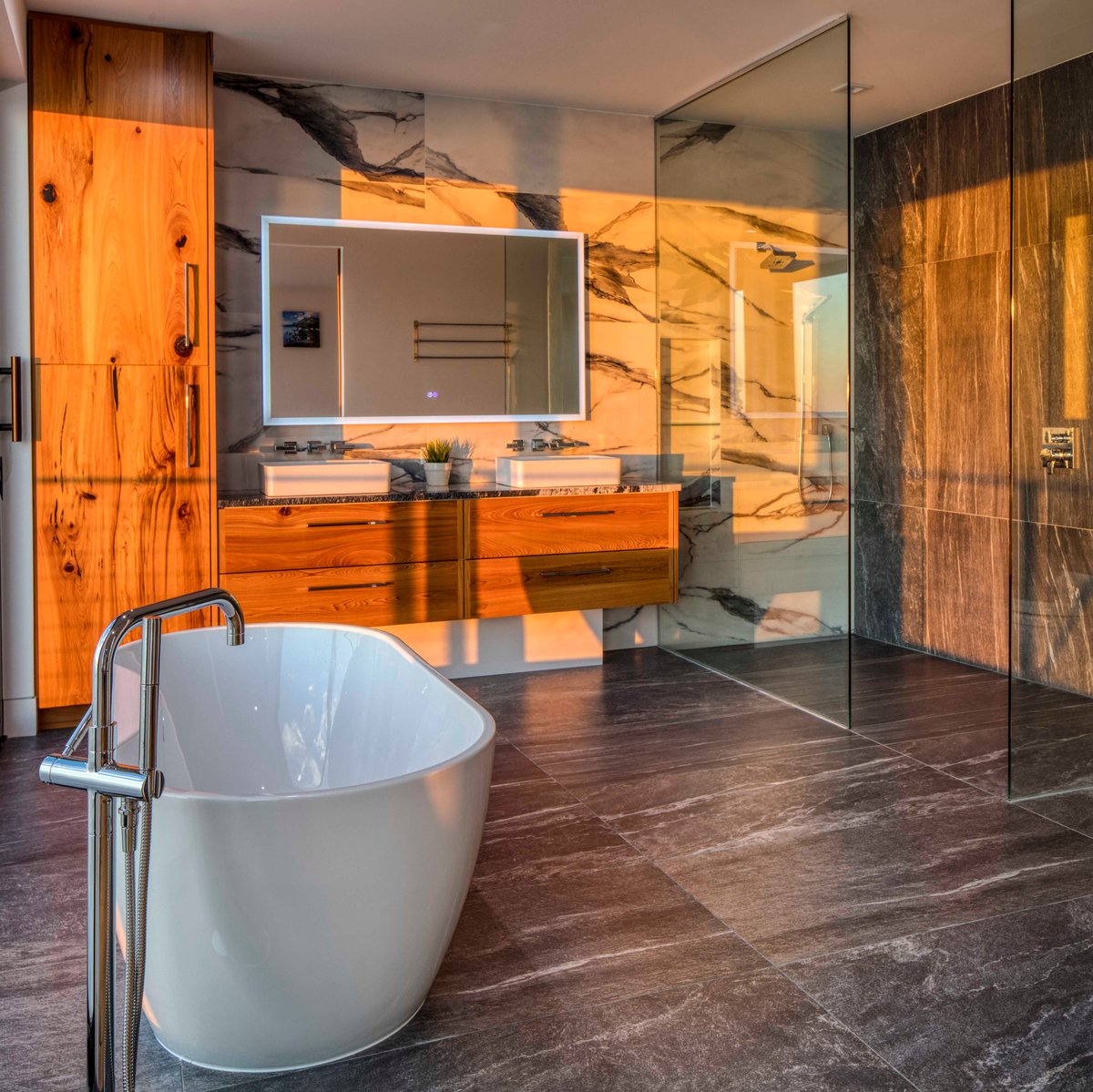 Image of modern bathroom with white freestanding bathtub, wooden cabinetry with vanity and large walk-in shower with large glass panel
