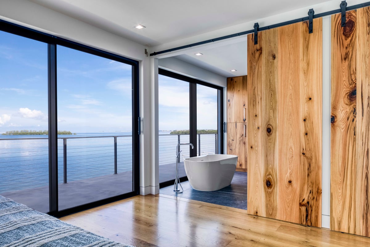 Image of modern bathroom with white free standing bathtub, wooden barn doors and wood plank floors